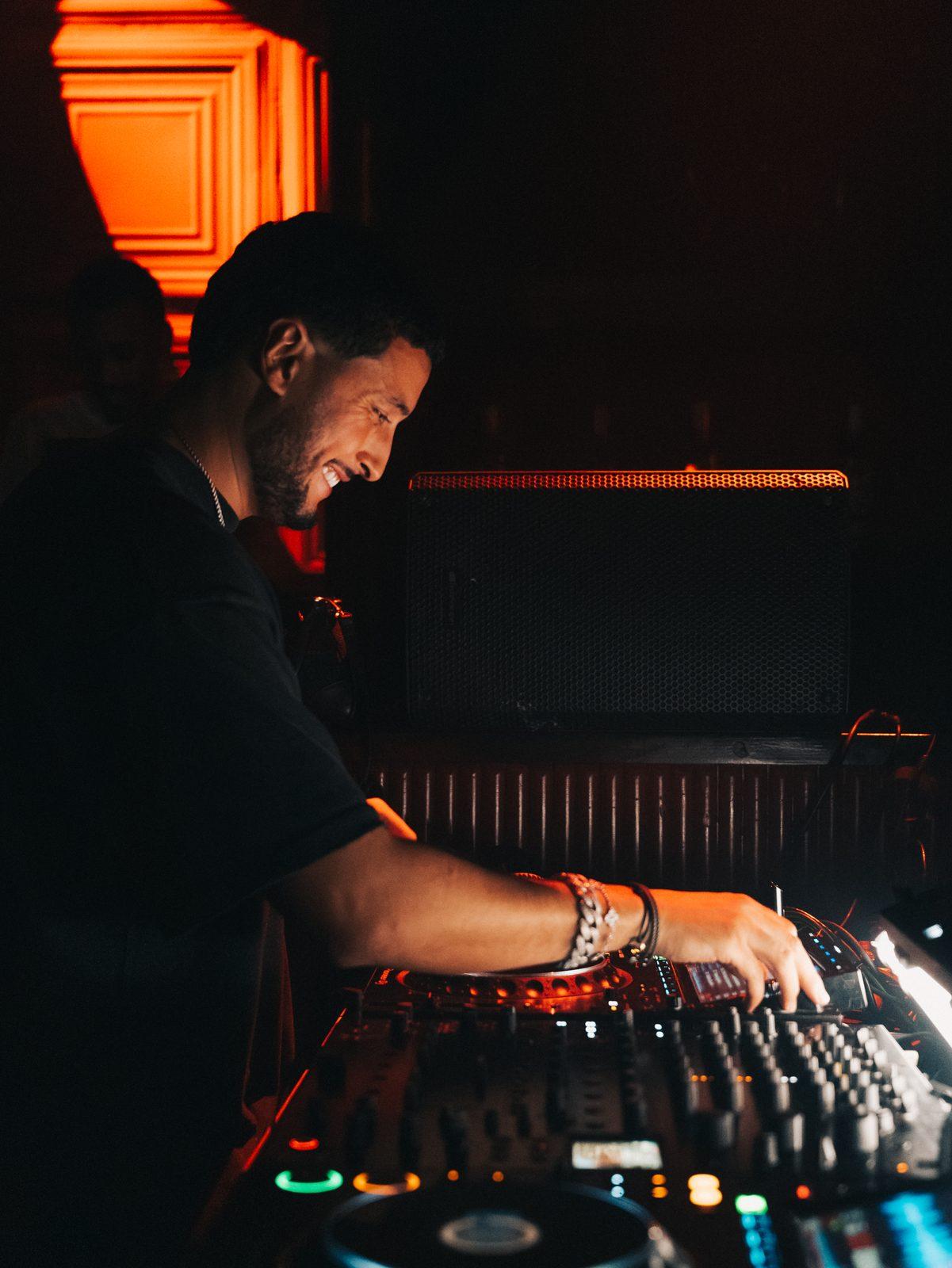 Saffou mixing in red light, smiling at the decks